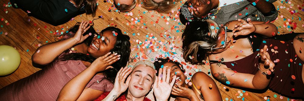 Group of diverse friends celebrating, lying on the floor with confetti. Smiling, joyful, diverse group enjoying a festive…