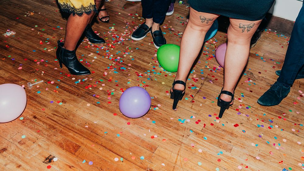 Party scene with colorful balloons and confetti on a wooden floor. People in stylish shoes, including high heels and boots…