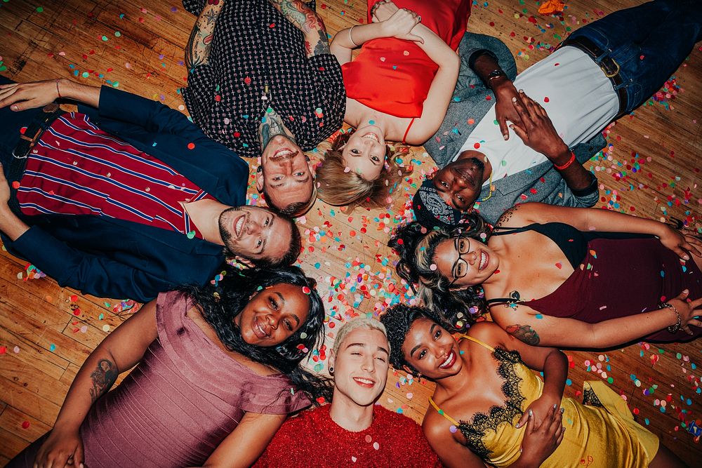 Diverse group of people lying on the floor, surrounded by confetti. Smiling men and women, various ethnicities, enjoying a…