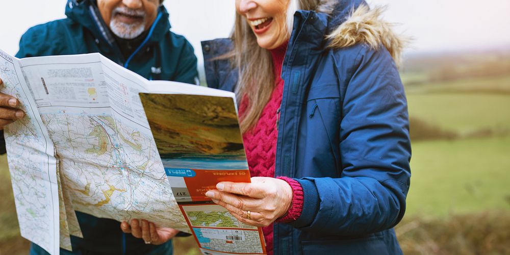 Elderly couple reading a map outdoors while traveling. Smiling elderly woman, old man with a beard. Exploring, map reading…