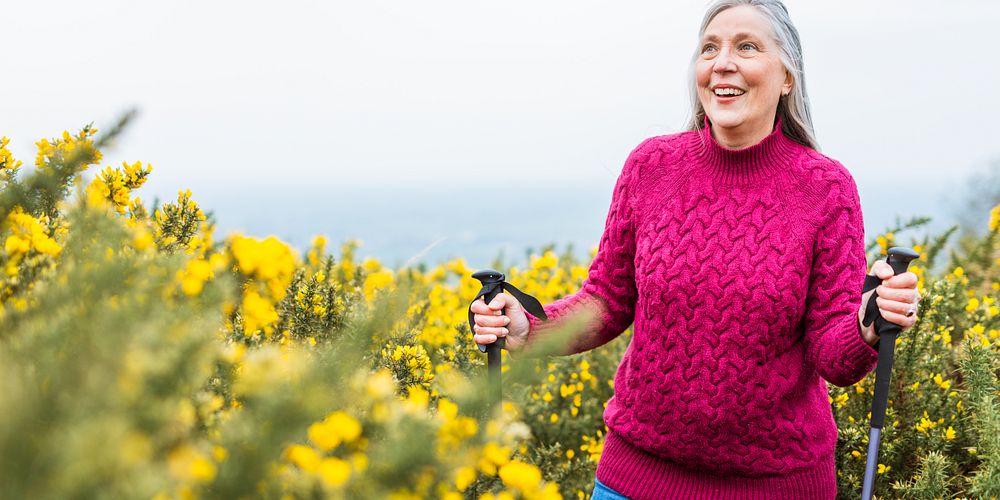 Elderly woman hiking with poles, smiling in nature. Elderly woman enjoying outdoor activity. Elderly woman in a red sweater…