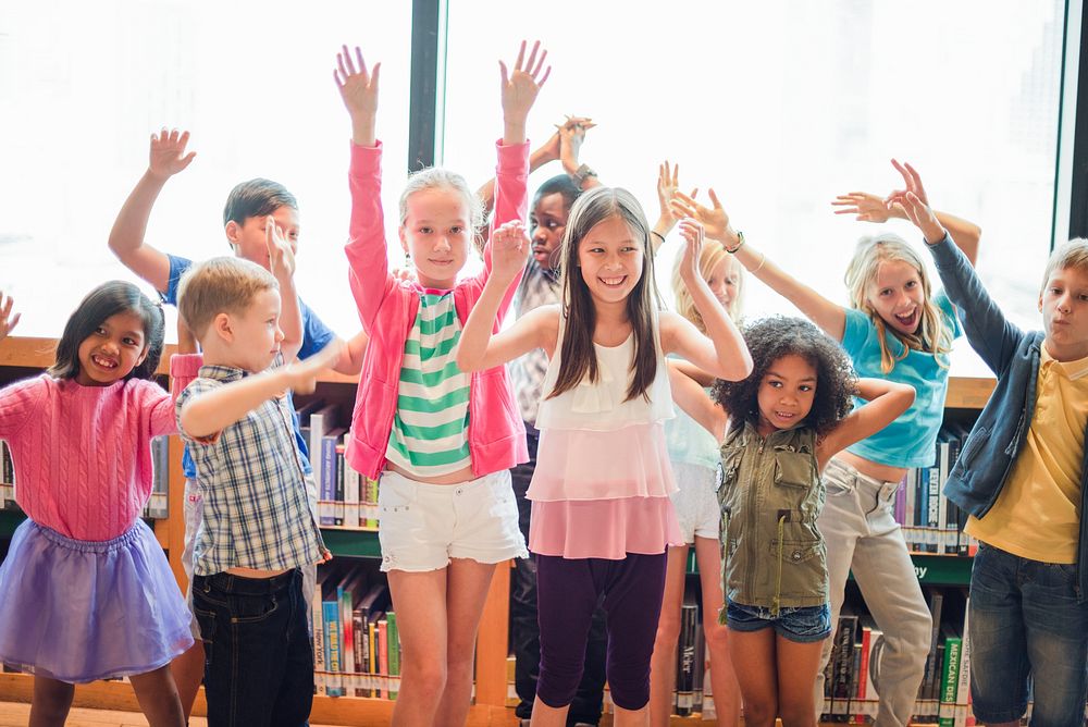 Group of diverse children having fun in a library. Kids smiling, raising hands, and enjoying their time. Happy children…