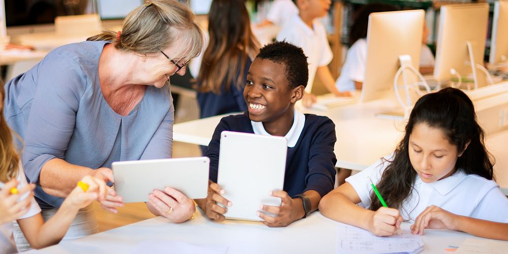 Teacher and students in a classroom with tablets. Diverse group learning with technology. Engaged students and supportive…