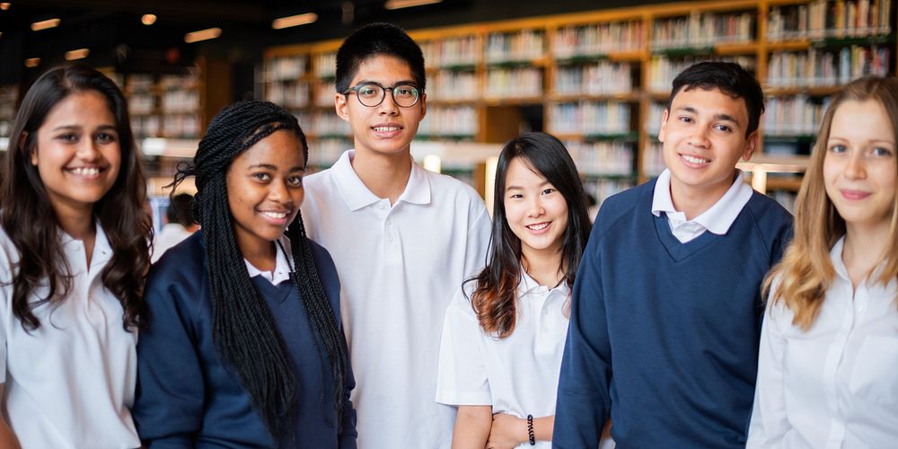 Group of diverse students in a library, wearing uniforms, smiling. Students in a library setting, diverse group, wearing…