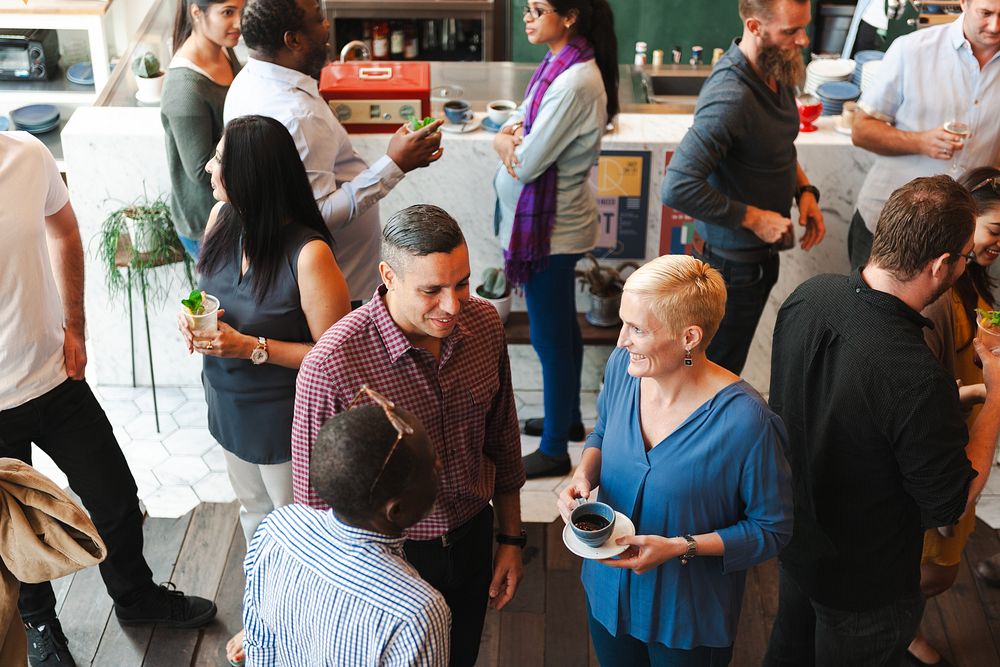 A diverse group of people socializing at a casual gathering. Men and women of various ethnicities are chatting and enjoying…