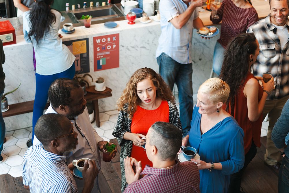 Diverse group socializing at a cafe. People chatting, holding drinks. Casual gathering, lively atmosphere. Group enjoying…