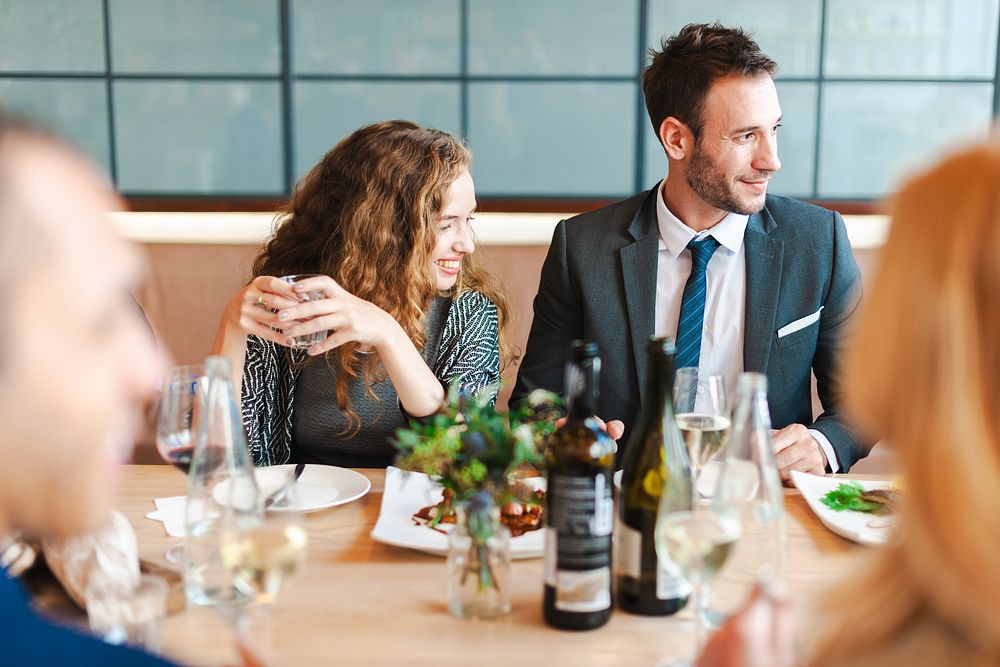 Group of business people dining at a restaurant. Two people smiling, enjoying a meal and wine. Casual business dining…