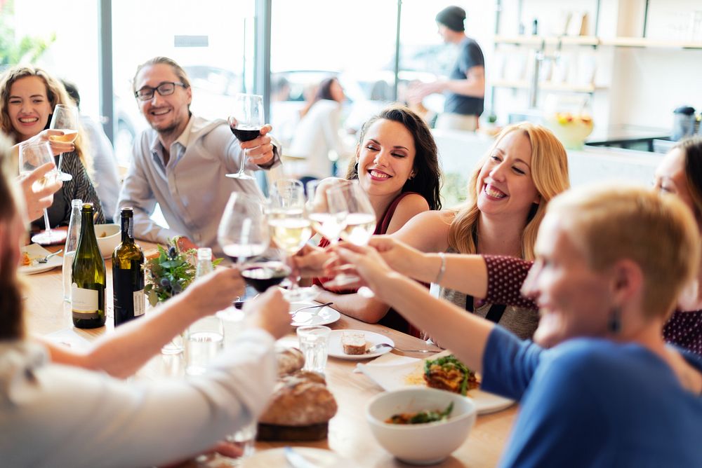 Group of people enjoying a meal, raising glasses in a toast. Diverse group celebrating, smiling, and dining together in a…