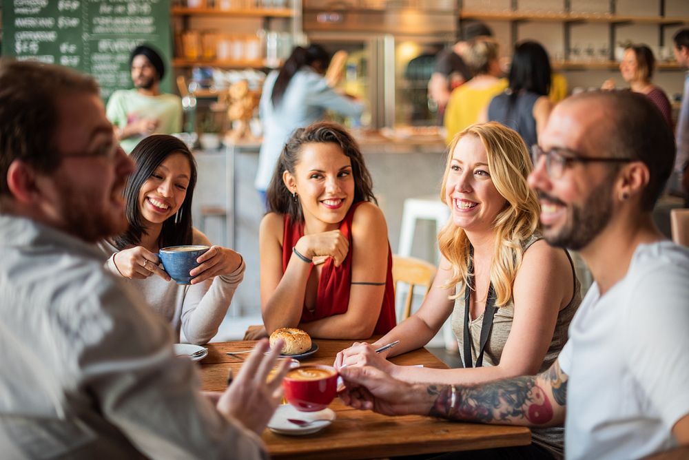 Group of friends enjoying coffee at a cafe. Smiling and chatting. Diverse group in a cozy cafe. Happy diverse friends having…