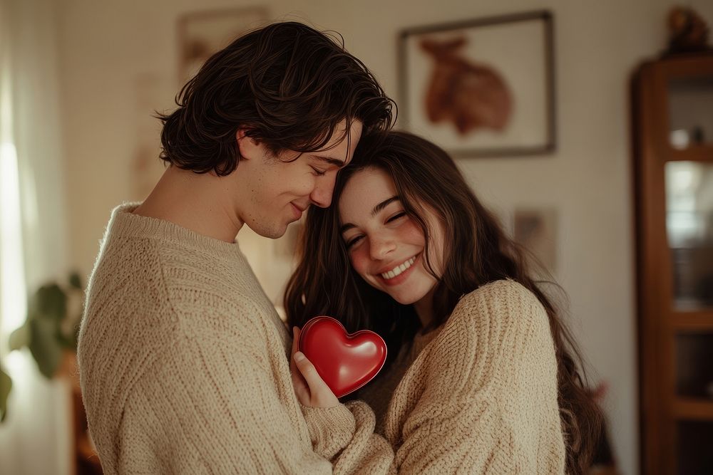 A caucasian man gives his girlfriend a red heart-shaped chocolate box sweaters happy smile.