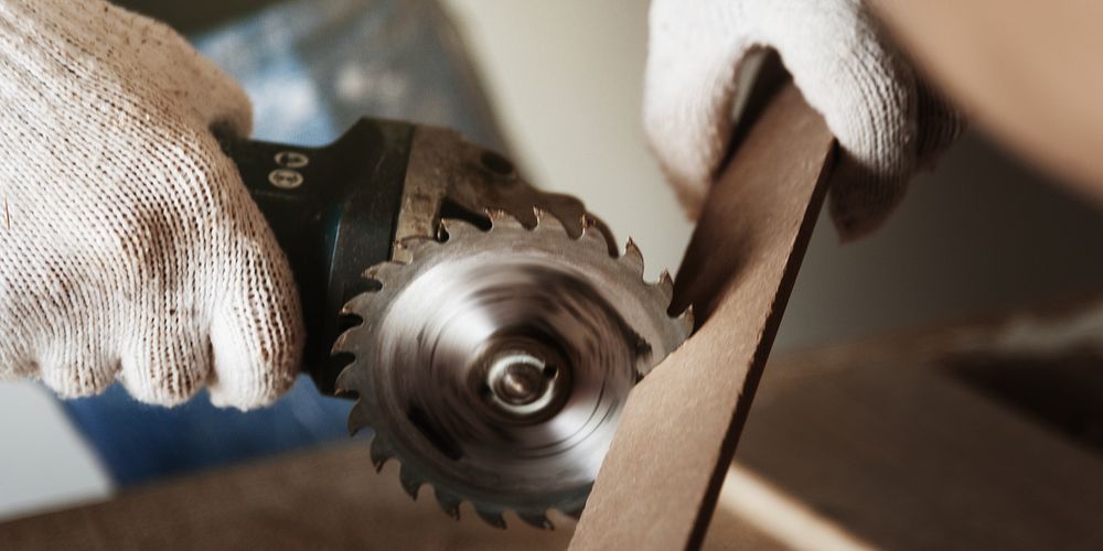 Close-up of hands using a circular saw to cut wood. The saw blade spins as it cuts through the wood. Protective gloves are…