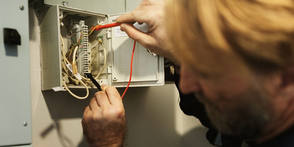 A man working on electrical wiring, adjusting cables in circuit box. Electrical work involves careful handling of wires and…