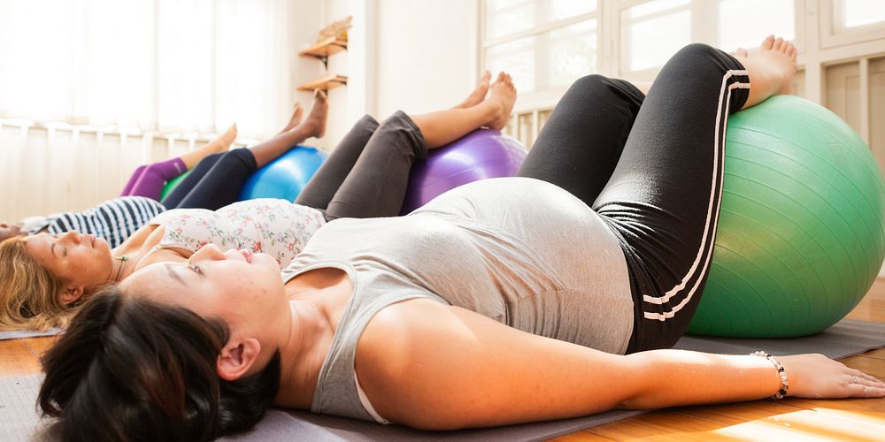 Pregnant women exercising with fitness balls in a bright room. Diverse group of women, prenatal fitness, relaxation, and…