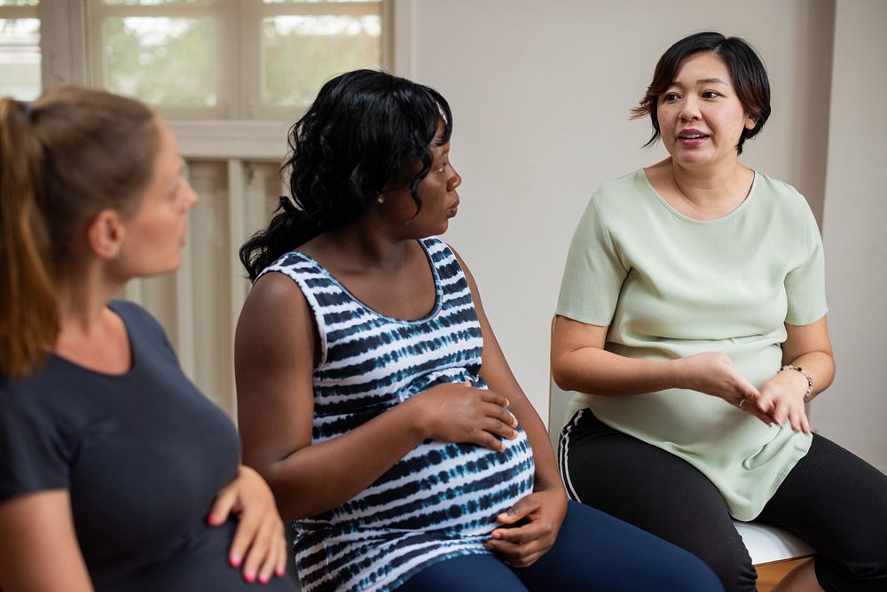 Three pregnant women sitting and talking in a casual setting, sharing experiences and advice. Diverse group engaged in a…