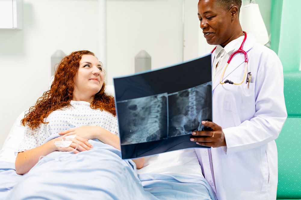 A doctor shows a patient an X-ray. The doctor, wearing a white coat, discusses the X-ray with patient in a hospital room.…