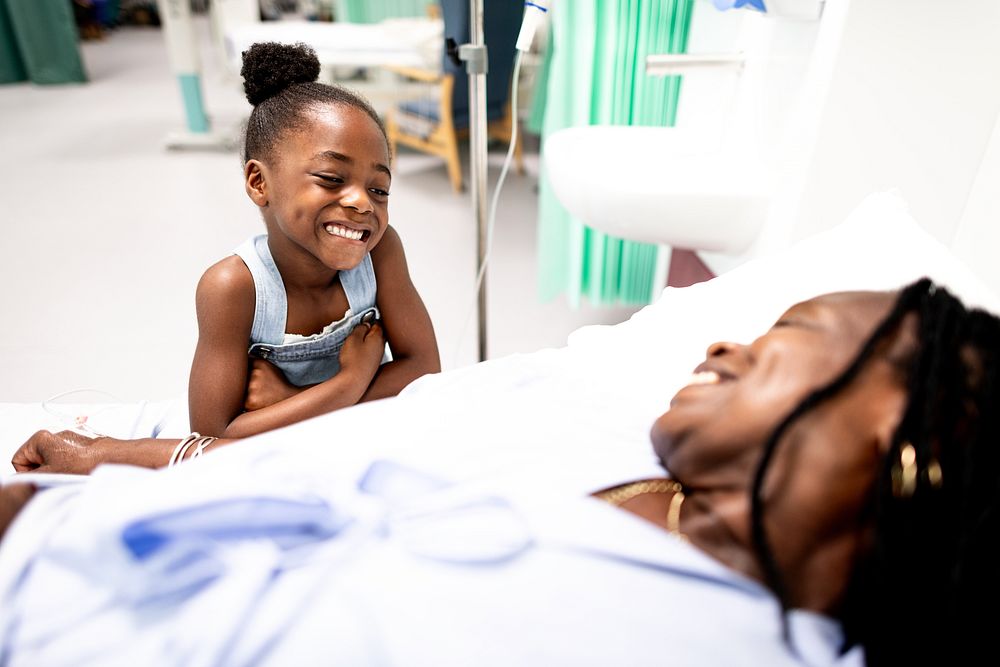 A child smiles at a person in a hospital bed, conveying warmth and care in a medical setting. The scene highlights family…