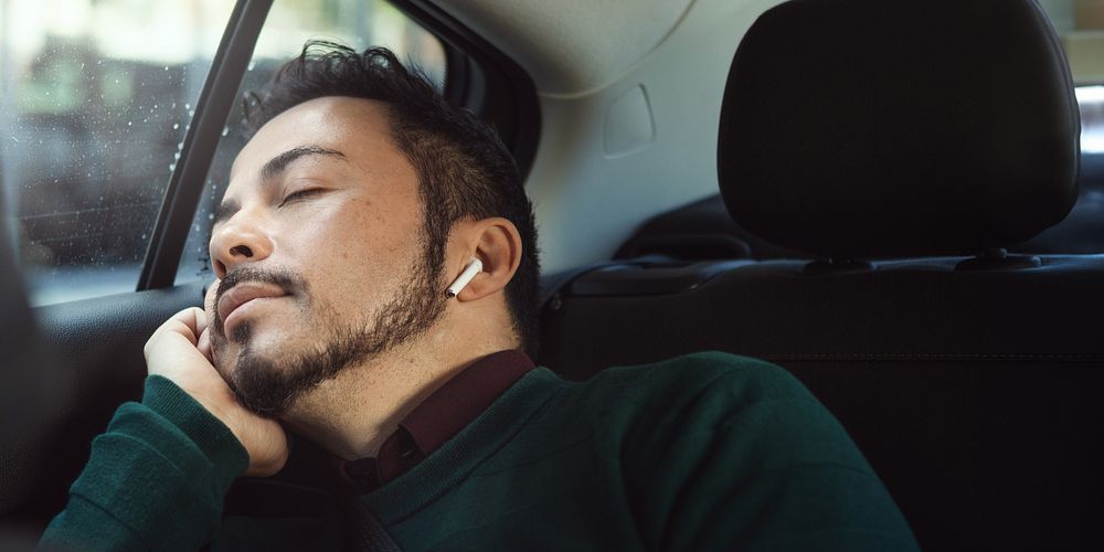 Man sleeping in car, wearing earbuds. Relaxed man resting, peaceful expression. Passenger seat, cozy atmosphere. Man…