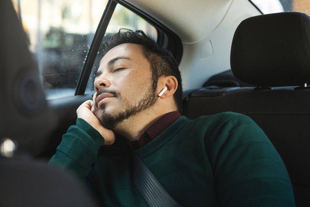 Man sleeping in car, wearing earbuds. Relaxed man, peaceful expression. Passenger seat, man resting. Casual attire, serene…