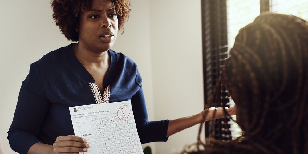 A woman shows a graded paper with an 'F' to another person. The woman appears concerned, discussing the failing grade. The…