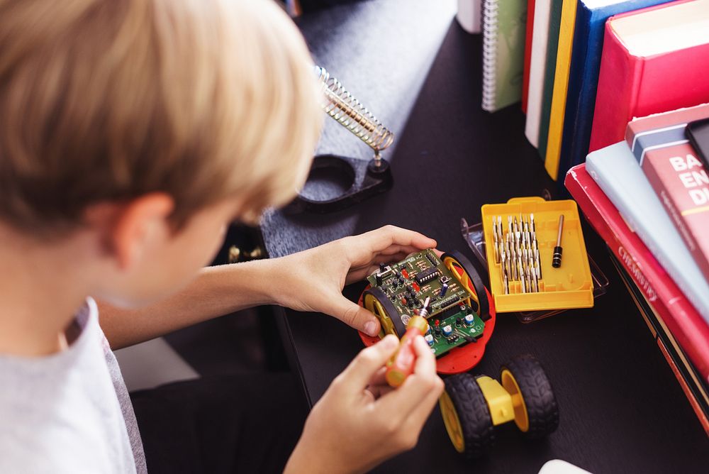 Young boy working on a small robot, using tools to assemble electronic parts. Focused on robotics, electronics, and…