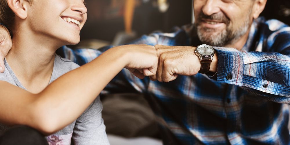 A joyful moment of connection between two father and son, showing a fist bump. Smiling faces, casual attire, and a sense of…