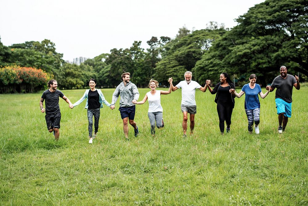 Diverse group of people holding hands in a park. Men and women of various ethnicities enjoying nature. Smiling, unity, and…