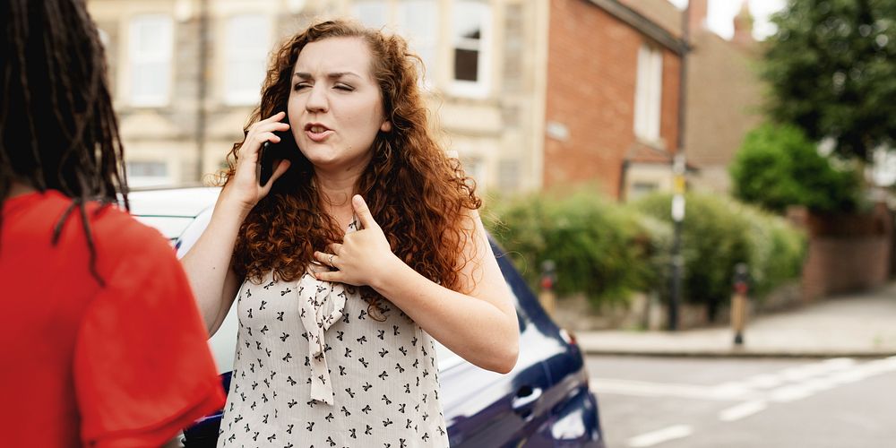 Woman with curly hair talking on phone, calling car insurance, standing on street. Expressive conversation, urban setting.…