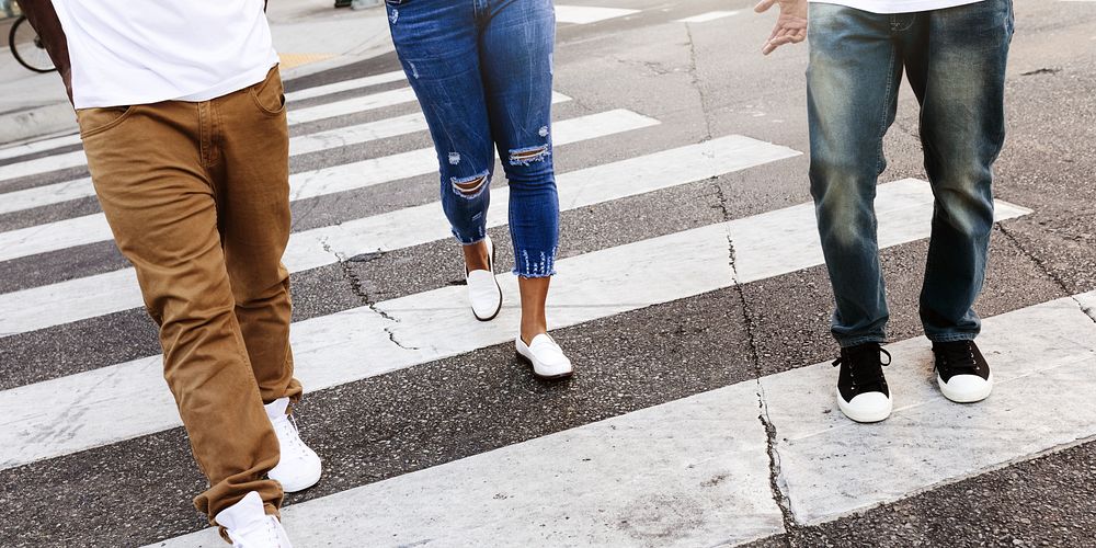 Three people walking on a crosswalk, wearing casual jeans and sneakers. Urban street scene with diverse individuals in…