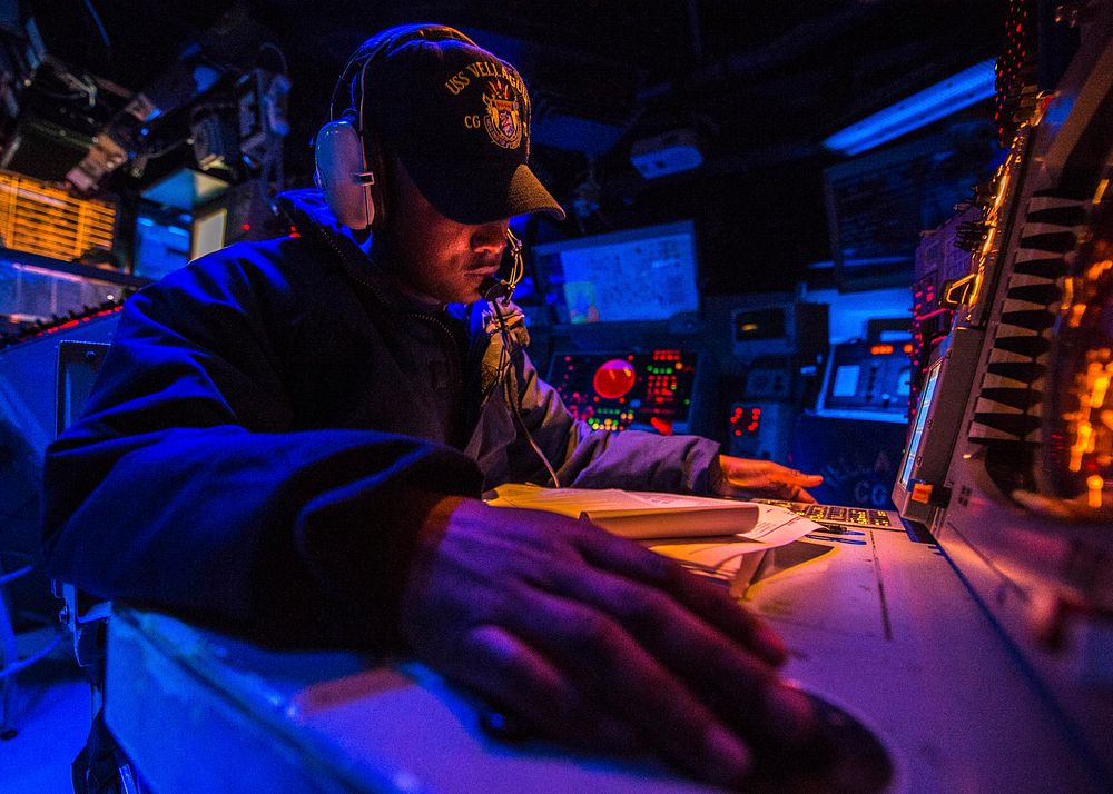 U.S. Navy Operations Specialist 2nd Class Paul Davis mans a watch station in the combat information center aboard the guided…