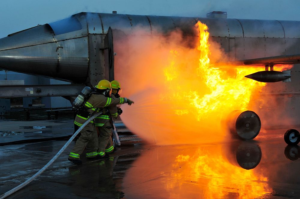 U.S. Navy firefighters and emergency services extinguish a simulated fire on a vehicle fire trainer at the firefighting…
