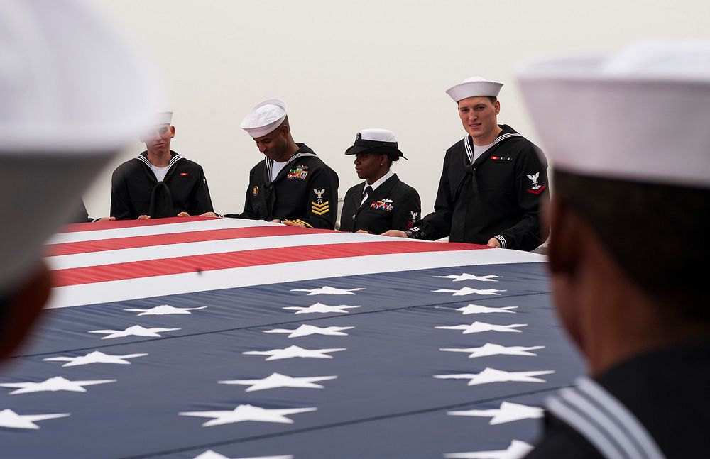U.S. Sailors assigned to the amphibious assault ship USS America (LHA 6) hold a U.S. flag for an aerial photo as the ship…