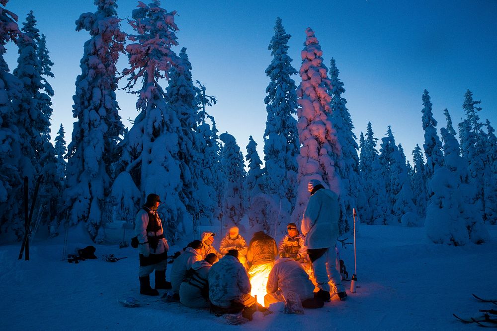 Participants of the Swedish Basic Winter Warfare Course rest in front of a fire during the course's culminating event in…