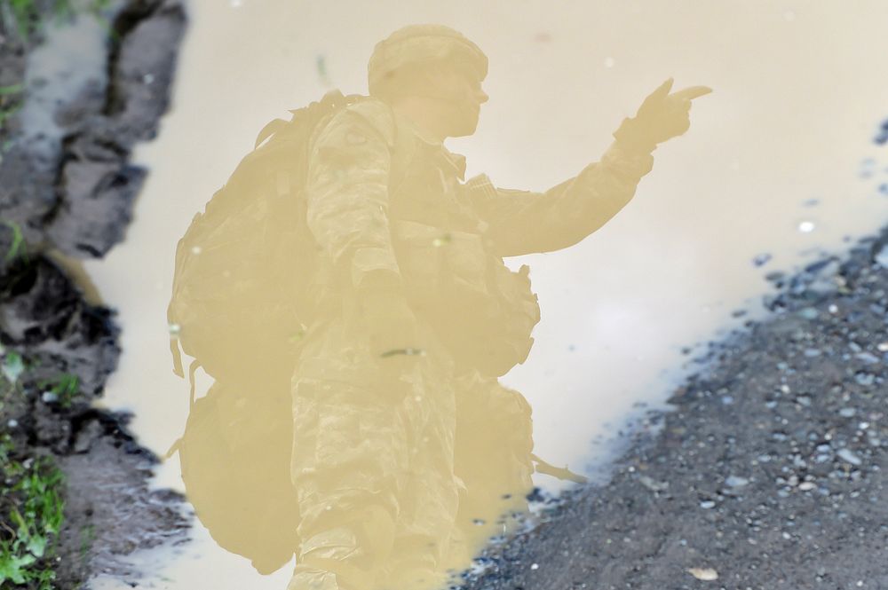 An officer is seen reflected in a pool of muddy water as he gives orders to fellow Soldiers assigned to the 4th Infantry…