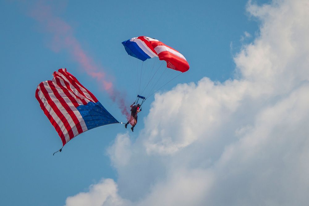 A member of the Patriot Parachute Team drops in with the American Flag in tow to start the afternoon airshow, July 24, 2018.