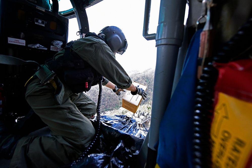 U.S. Coast Guard Petty Officer 2nd Class Kenneth Krowel drops a box of MRE's to locals from a Coast Guard MH-65 Dolphin…