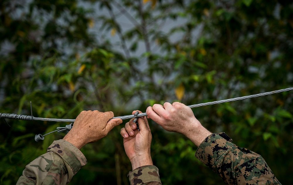 U.S. Army Maj. Robert Vandertuin, left, and U.S. Marine Maj. Jeremy Carroll fix a wire on a fence that helps mitigate…