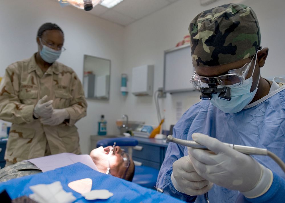 U.S. Navy Lt. Cmdr. Rodney Scott, a dentist, prepares an amalgam filling as Hospital Corpsman 3rd Class Shaunta Johnson, his…