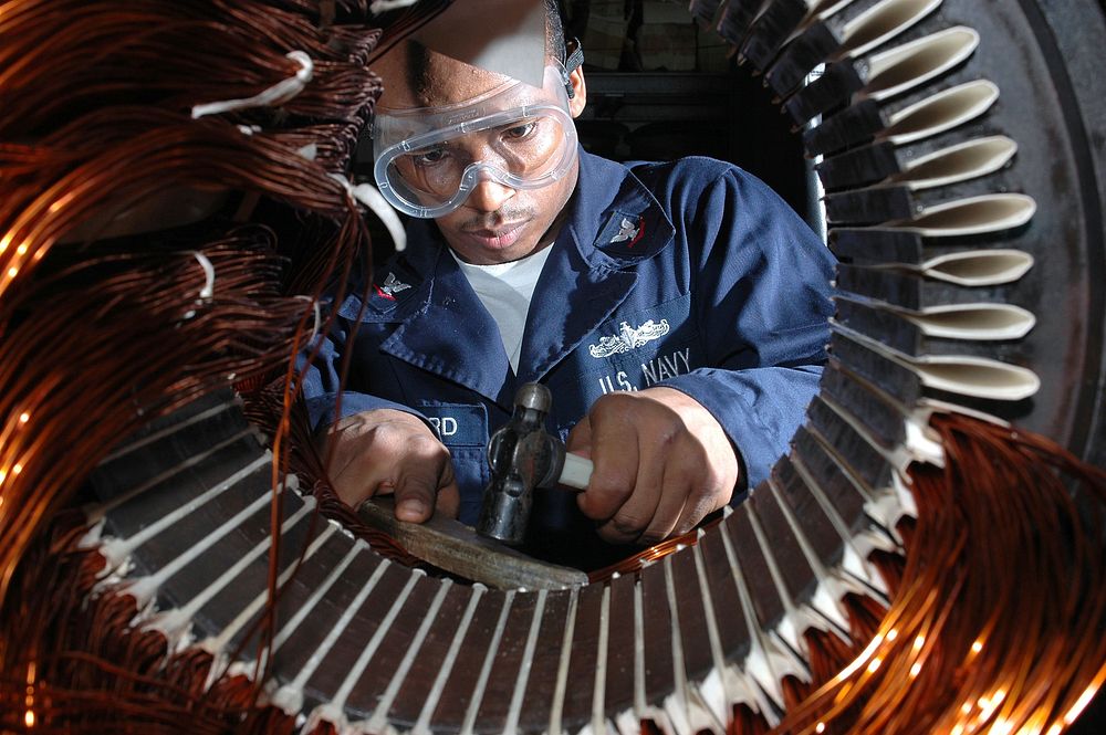 U.S. Navy Electricians Mate 3rd Class Tyreek Hayward lays coil to rewind a motor in the machine shop aboard the aircraft…