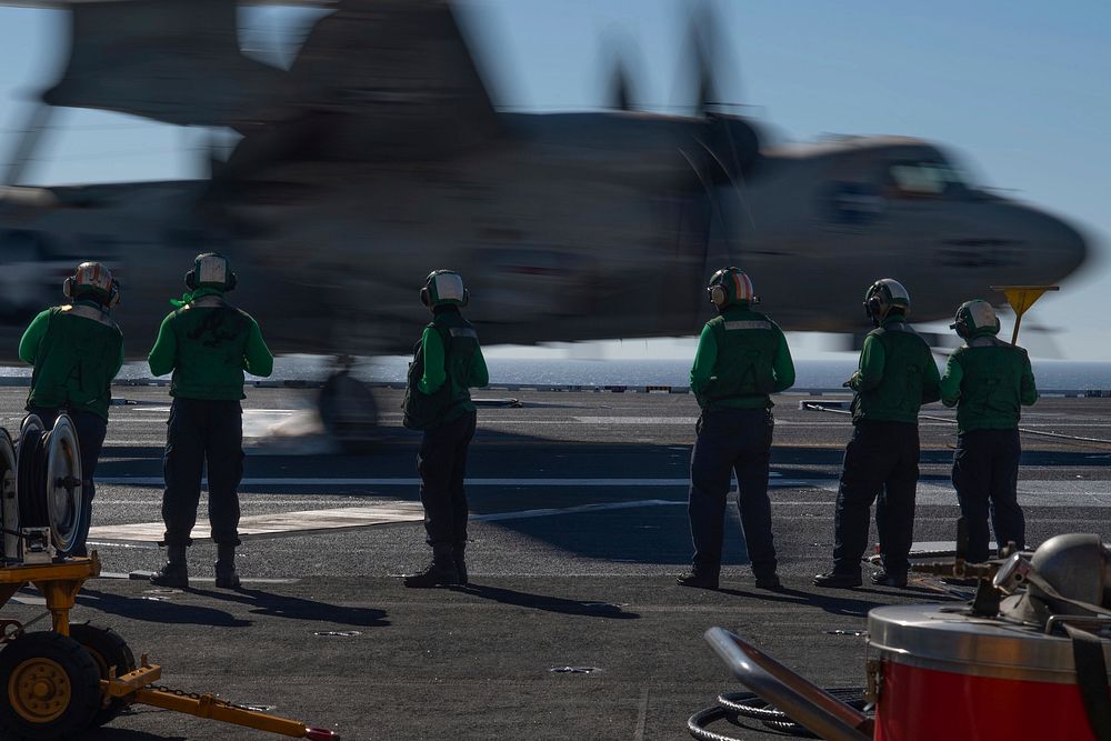 U.S. Sailors observe an E-2C Hawkeye attached to Carrier Airborne Early Warning Squadron (VAW) 117 as it lands on the flight…