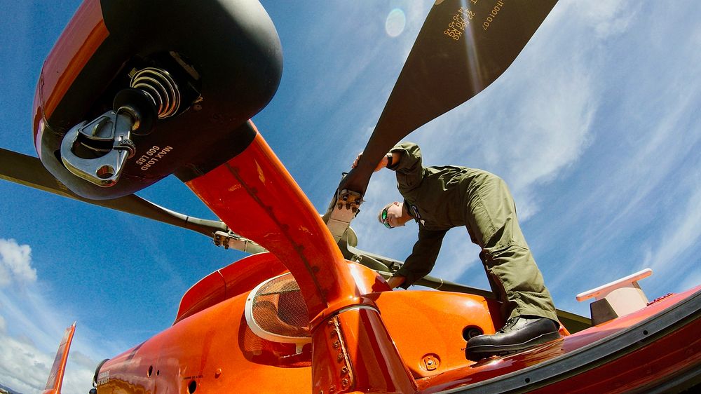 An aircrew member from Coast Guard Air Station Barbers Point rotates the rotor on an MH-65 Dolphin helicopter following a…