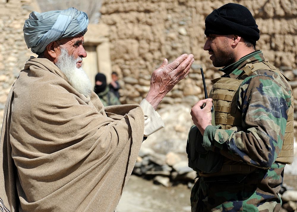An Afghan National Army (ANA) commando, right, conducts a key leader engagement with an Afghan village elder during a…