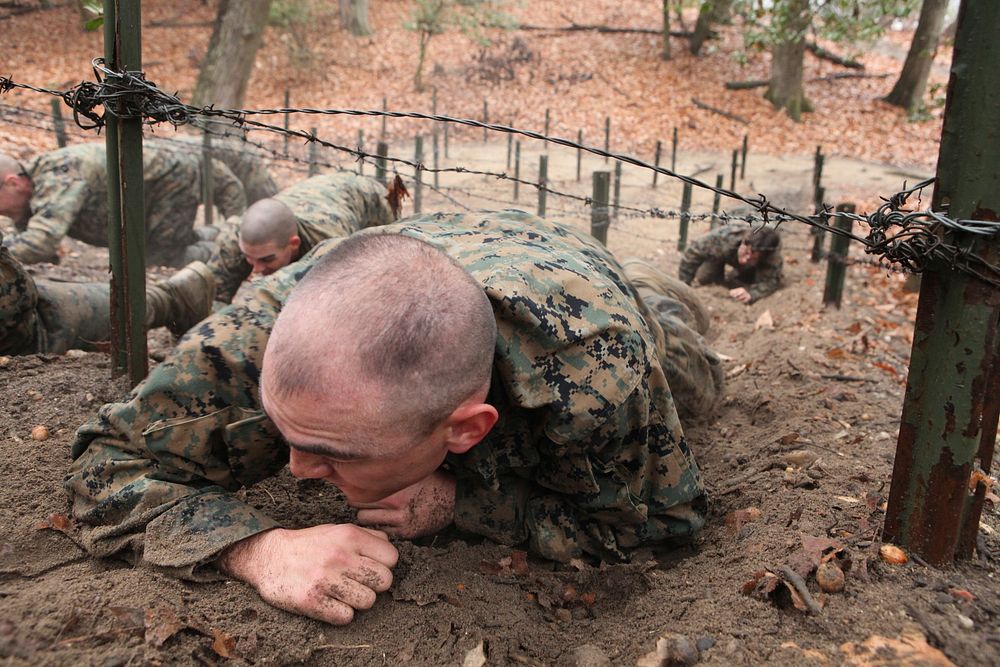 A U.S. Marine enrolled in Officer Candidate School low-crawls under a barbed wire obstacle on the Montford Point Challenge…