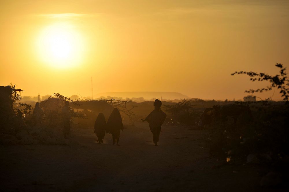 A woman and two girls walk through an IDP camp on the outskirts of Beled Weyne. Original public domain image from Flickr
