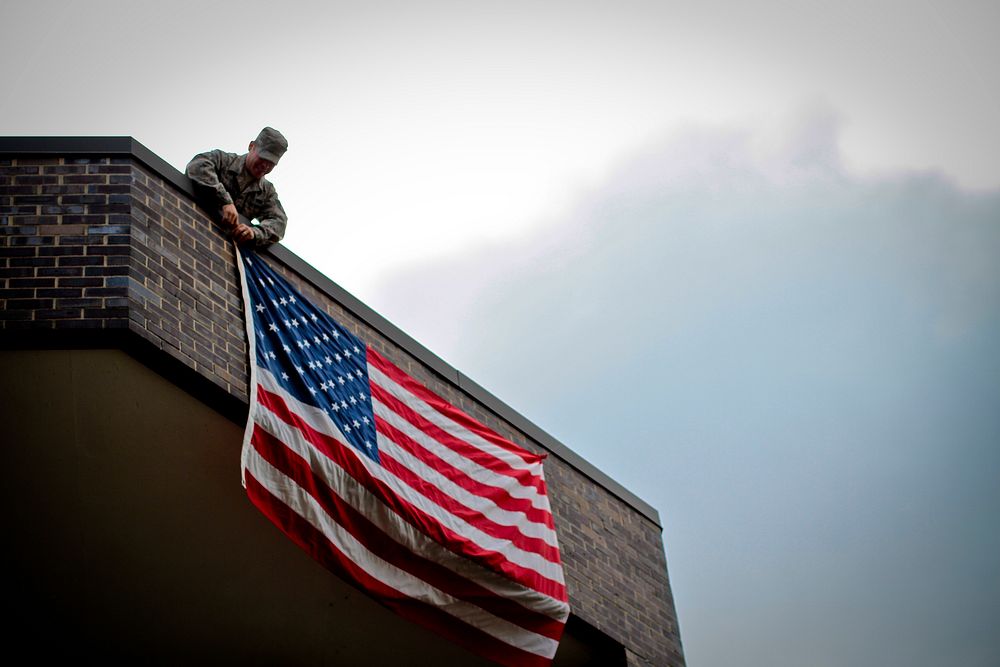 New Jersey Air National Guardsman Staff Sgt. Randy Garrison secures an American flag onto a building being converted to…