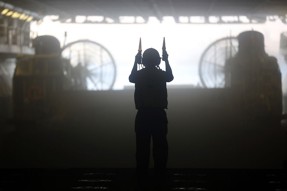 A U.S. Navy boatswain's mate directs a landing craft air cushion in the well deck of the amphibious assault ship USS…