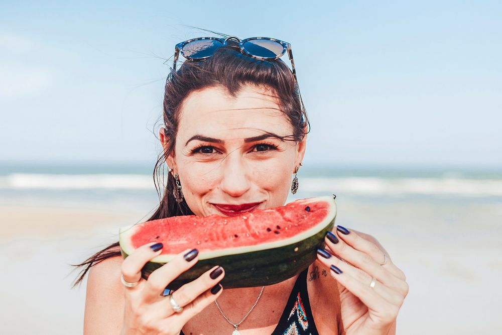 Woman eating watermelon at the beach, bright blue tone