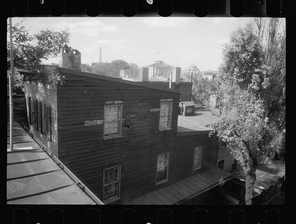 [Untitled photo, possibly related to: Old wooden shacks on left of picture. Many of these houses have no inside water supply…