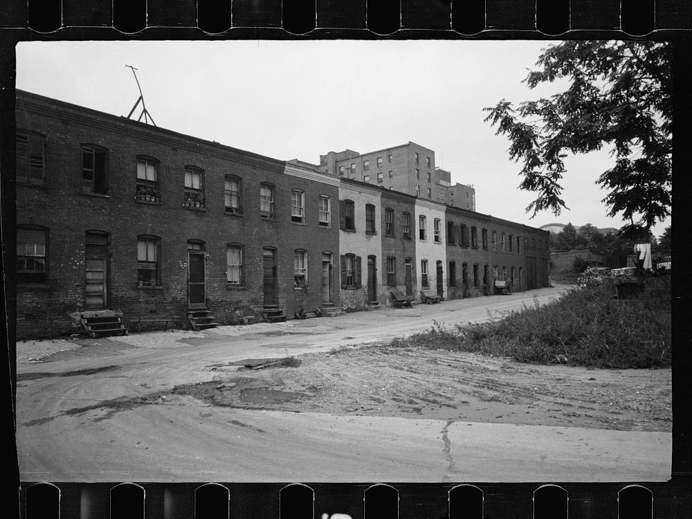 Block of slum houses with outside toilets and water supply, hotel to the left and the round roof of Union Station in the…