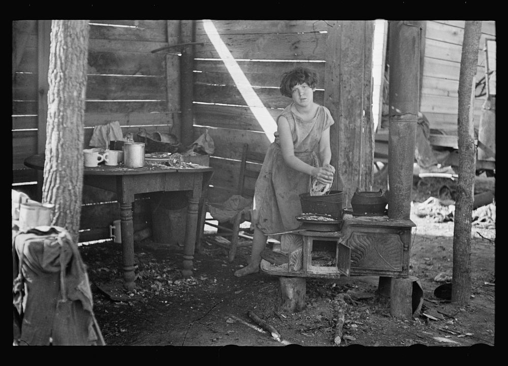 Twelve-year old girl of family of nine, cooking meal in rude, open lean-to near hut, Tennessee. Sourced from the Library of…