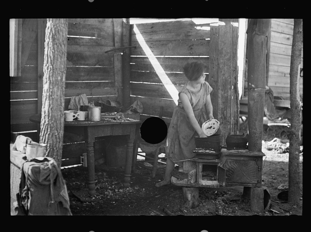 [Untitled photo, possibly related to: Twelve-year old girl of family of nine, cooking meal in rude, open lean-to near hut…